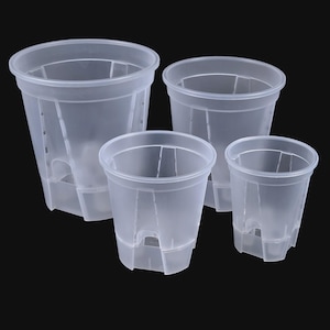 Può includere: Quattro vasi di plastica trasparente di diverse dimensioni sono disposti su uno sfondo nero. I vasi hanno una forma cilindrica con fessure verticali e fori di drenaggio sul fondo. Questi vasi sono progettati per le piante.