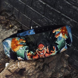 May include: A black dog collar with a vibrant anime-style illustration of a character with black hair, red skin, and orange and green details. The collar has a blue interior and a silver buckle.