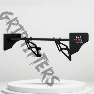 May include: A black car spoiler with a GT logo in red. The spoiler has a horizontal bar with supporting brackets and vertical end pieces. The product is designed for automotive use.