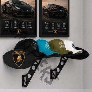 May include: A black wall shelf displays five baseball caps with various designs and colors, including a black cap with a white logo, a blue cap with a maple leaf, and a white cap. Two framed car posters are above the shelf.