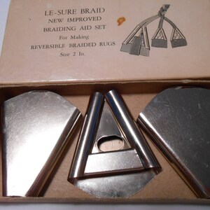 May include: A set of three metal braiding tools in a cardboard box. The box has the text "LE-SURE BRAID NEW IMPROVED BRAIDING AID SET For Making REVERSIBLE BRAIDED RUGS Size 2 In."