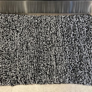 May include: Black and white bath mat with a fluffy texture. The mat is made of a soft, absorbent material and is perfect for drying your feet after a shower or bath.