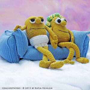 以下が含まれることがあります： 黄色いジャガイモに似た2つの手作りの編み物フィギュアが、青い編み物のソファに座っています。1つのフィギュアは白いおむつを着用しています。フィギュアは黒い目を持ち、白い表面に休んでいます。「- COUCHPOTATOES - © 2013 BY KATJA HEINLEIN」というテキストが下にあります。
