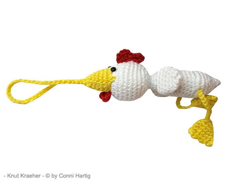 May include: A handmade, whimsical crochet chicken toy. The chicken features a white body, yellow beak and feet, and a red comb and wattle. A yellow loop extends from the beak. The toy is designed with a cartoonish aesthetic.