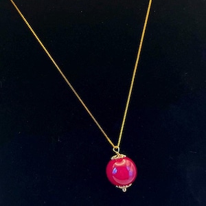 May include: A gold chain necklace with a large, round, red pendant. The pendant is smooth and shiny.