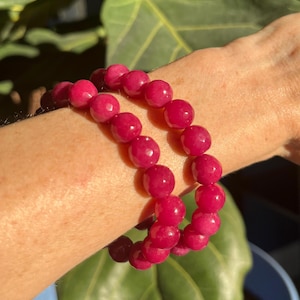 May include: Two pink gemstone bracelets with round beads. The bracelets are stacked on a person's wrist.