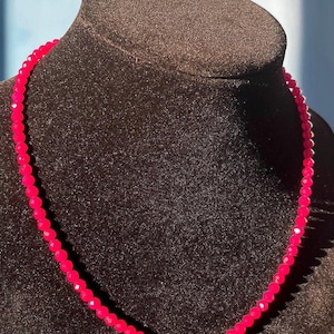 May include: A pink beaded necklace on a brown velvet mannequin bust.