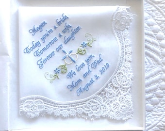 May include: A white handkerchief with delicate lace trim, presented in a box. The handkerchief features blue embroidered text: "Megan, Today you're a bride, Tomorrow a wife, Forever our daughter. We love you, Mom and Dad, August 3, 2019."