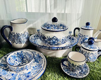 Może przedstawiać: Zestaw niebieskich i białych ceramicznych filiżanek do herbaty, czajnika, dzbanka na śmietanę, cukiernicy i talerza do serwowania z kwiatowymi wzorami. Zestaw jest ułożony na zielonej powierzchni.