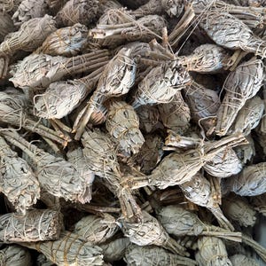 May include: A close-up view of a bundle of white sage smudge sticks. The sticks are tied together with twine and are ready to be used for smudging rituals.