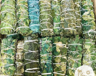 May include: A close-up view of a box filled with bundles of dried herbs, tied with twine. The bundles are various shades of green and are arranged in rows. The box is made of cardboard and has a brown colour.