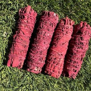 May include: Four red sage smudge sticks bundled together. The sticks are wrapped in red string and have a natural, earthy look.