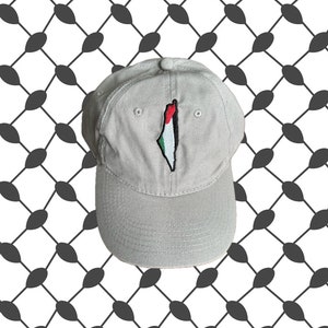 Puede incluir: Una gorra de béisbol gris con una bandera palestina bordada en la parte delantera. La bandera es roja, verde, negra y blanca.