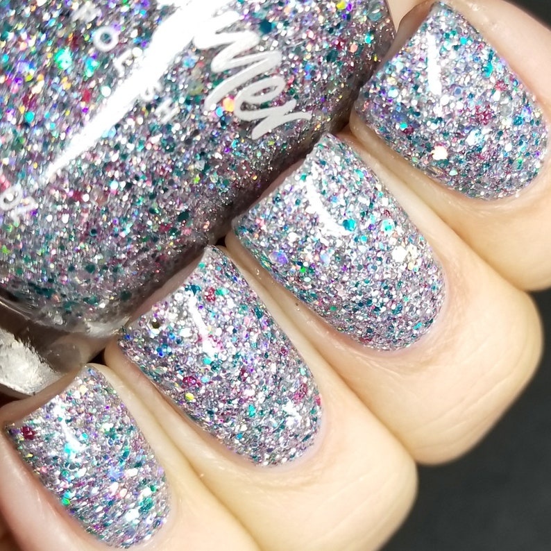 Puede incluir: Primer plano de cuatro u&ntilde;as pintadas con un esmalte de u&ntilde;as de brillo plateado. El esmalte tiene una variedad de brillos de colores, incluyendo rosa, azul y verde.