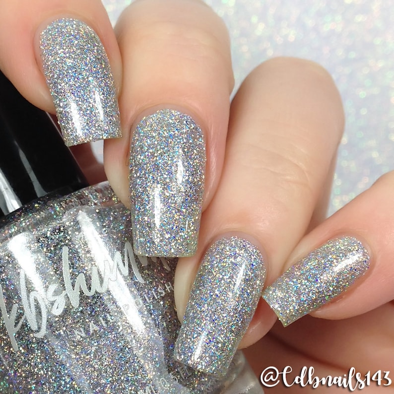 May include: A bottle of silver glitter nail polish with a black cap. The bottle is labeled "KBShimmer Nail Polish".