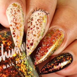 May include: Close-up of a hand with several nails painted with a beige base and a holographic, iridescent, gold and red glitter top coat. The nails are long and pointed. The hand is holding a bottle of nail polish with a holographic, iridescent, gold and red glitter finish. The bottle is labeled "Shimmer Nail Polish".
