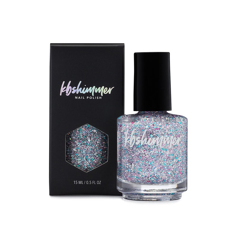 Puede incluir: Una botella de esmalte de u&ntilde;as con purpurina iridiscente con una tapa negra y una etiqueta que dice "kb shimmer nail polish". La botella est&aacute; sobre una superficie blanca.