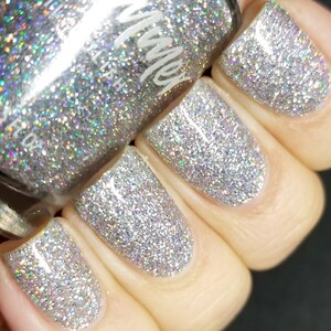 May include: Close-up of a hand wearing silver glitter nail polish. The polish is a fine glitter with a holographic effect. The bottle of nail polish is visible in the background.