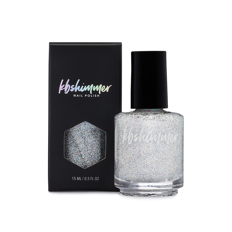 May include: A bottle of silver glitter nail polish with a black cap. The bottle is labeled "kb shimmer nail polish" and has a hexagonal shape with a silver glitter design. The bottle is 15 ml / 0.5 fl oz.