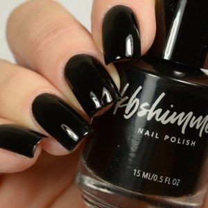 May include: Black nail polish bottle with the brand name "kb shimmer" and the text "nail polish" and "15 ml/0.5 fl oz". The bottle is shown with black nail polish on four fingernails.