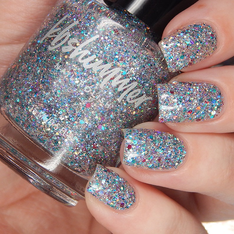 Puede incluir: Una botella de vidrio transparente de esmalte de u&ntilde;as con un acabado de brillo plateado. La botella est&aacute; etiquetada como "Kismet Nail Polish".