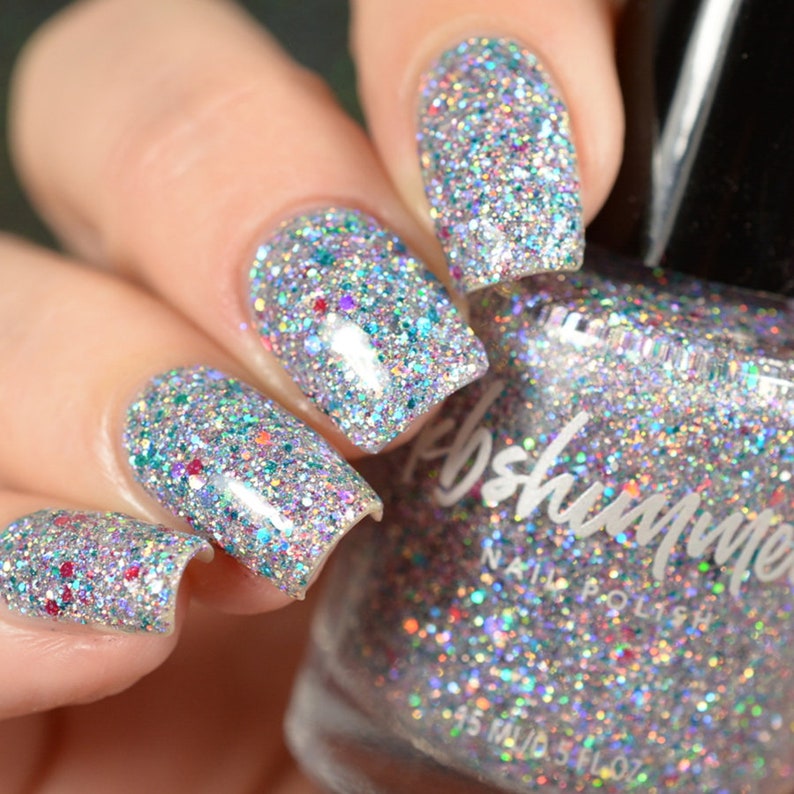 Puede incluir: Una botella de vidrio transparente de esmalte de u&ntilde;as con purpurina plateada con una etiqueta blanca que dice "Polish Me" y "Nail Polish". La botella est&aacute; sobre una mano con cuatro u&ntilde;as pintadas con el mismo esmalte de u&ntilde;as con purpurina plateada.