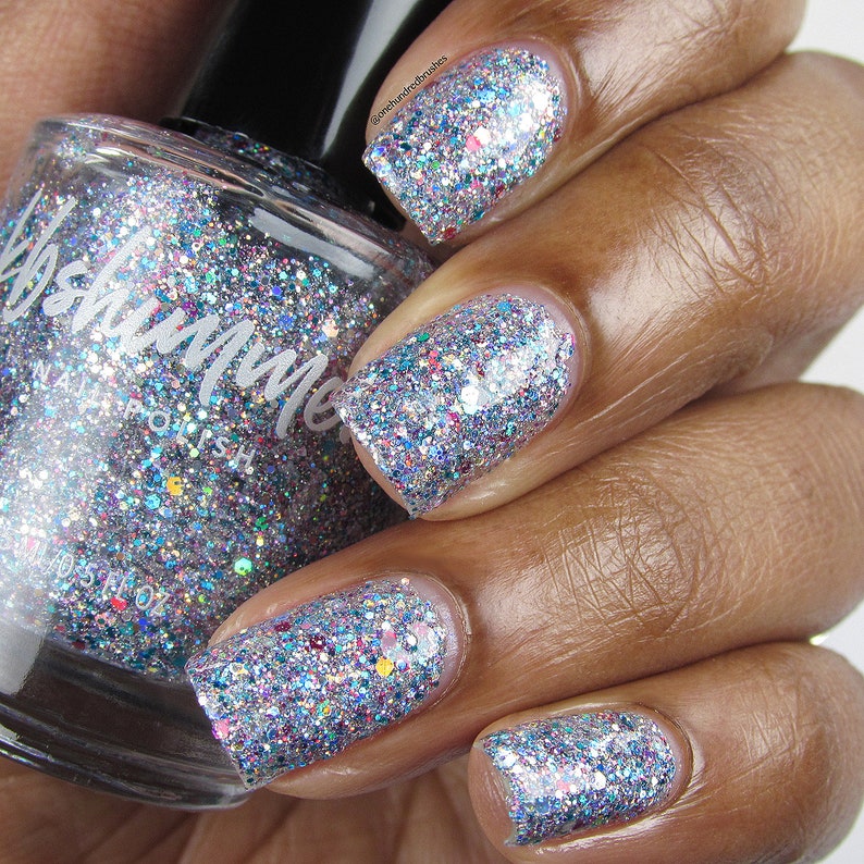 Puede incluir: Una botella de vidrio transparente de esmalte de u&ntilde;as de purpurina plateada con una tapa negra. La botella est&aacute; etiquetada como "#shimmer" esmalte de u&ntilde;as. Una mano lleva el esmalte de u&ntilde;as, que es una purpurina plateada con destellos azules, rosados y verdes.