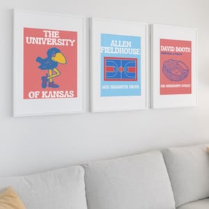 Könnte beinhalten: Drei gerahmte Drucke mit weißen Rahmen und weißem Hintergrund. Der Druck links zeigt einen roten Hintergrund mit einem blauen Vogelmaskottchen und dem Text "The University of Kansas". Der mittlere Druck zeigt einen blauen Hintergrund mit einem Basketballfeld und dem Text "Allen Fieldhouse 1651 Naismith Drive". Der Druck rechts zeigt einen roten Hintergrund mit einem Stadion und dem Text "David Booth Memorial Stadium 1101 Mississippi Street".