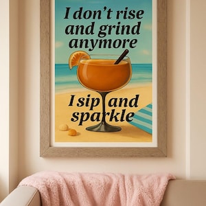 May include: Framed art print with a beach scene and a cocktail. The print features a large orange cocktail with a straw, a slice of orange, and the text "I don't rise and grind anymore. I sip and sparkle."