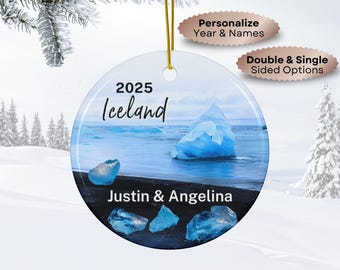 May include: A round Christmas ornament featuring a scenic Iceland landscape with icebergs and black sand. The ornament includes the year "2025", the word "Iceland", and the names "Justin & Angelina". It has a gold string for hanging.