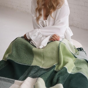 Könnte beinhalten: Eine grün-weiß karierte Decke mit Fransen. Die Decke besteht aus einem weichen Material und hat eine Vielzahl von Grüntönen. Die Decke ist gefaltet und über einer Person drapiert.