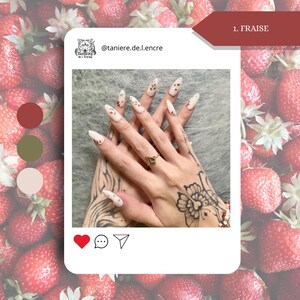 May include: A close-up of hands with long, almond-shaped nails. The nails are painted white with small red and green strawberry designs. The hands also have tattoos and a gold ring. The image is set against a background of strawberries.