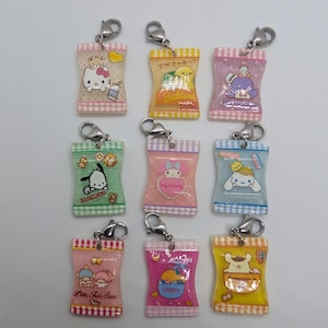 Puede incluir: Nueve llaveros coloridos con temática de dibujos animados en forma de bolsas de aperitivos. Cada amuleto presenta un personaje y un diseño diferente, con cierres plateados para la fijación. Los amuletos están dispuestos en tres filas de tres.