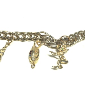 May include: A gold charm bracelet with a chain link design and multiple charms, including a seashell, a mermaid, a flower, and a fairy.