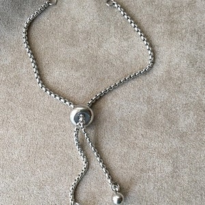 May include: A silver chain bracelet with a sliding clasp and two round beads at the ends.