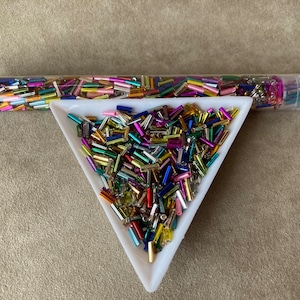 May include: A clear plastic tube filled with colorful metallic glass beads. The beads are in a variety of shapes and sizes. The tube is labeled "SK-M66B".