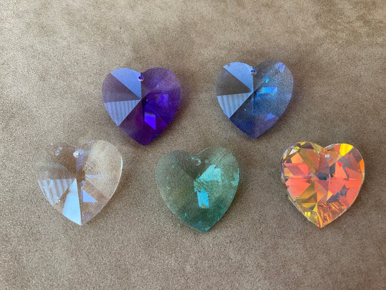 May include: Five heart-shaped crystal prisms in various colors, including clear, purple, blue, green, and orange. The prisms are faceted and have a hole at the top for hanging.