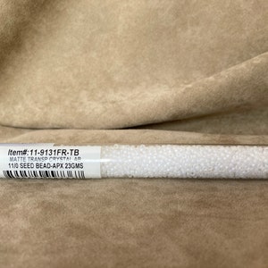 May include: A clear plastic tube filled with white seed beads. The label reads "Item#: 11-9131FR-TB Matte Transp Crystal AB 11/0 Seed Bead-Apx 23GMS".