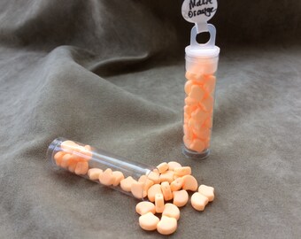 May include: Two small clear plastic tubes filled with peach-colored beads. The tubes have a white label with the text "Matte Orange". One tube is lying on its side with beads spilling out.