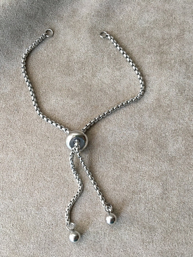 May include: A silver chain bracelet with a sliding clasp and two round beads at the ends.