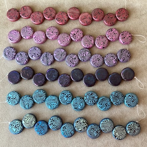 Könnte beinhalten: Sechs Reihen runder, flacher, bunter Perlen mit einem wirbelnden Schwarz-Weiß-Muster. Die Perlen sind auf weißem Faden aufgereiht.