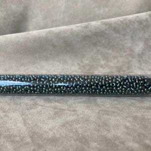 May include: A clear plastic tube filled with dark green seed beads. A white label with the text "BR - 459K" is attached to the tube.