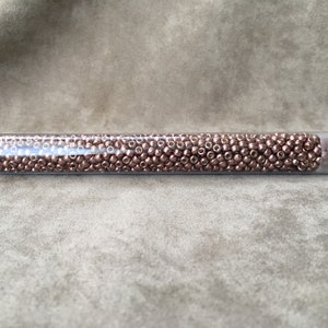 May include: A clear plastic tube filled with small, round, copper-colored beads. The tube has a white label with the text "8 P4190".