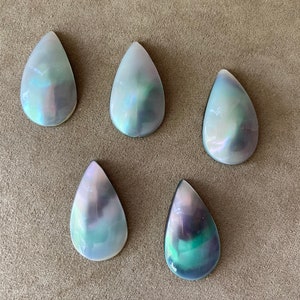 以下が含まれることがあります： 真珠光沢のある仕上げを施した、虹色の涙滴型のカボションが5つ。カボションは白、グレー、緑のミックスです。