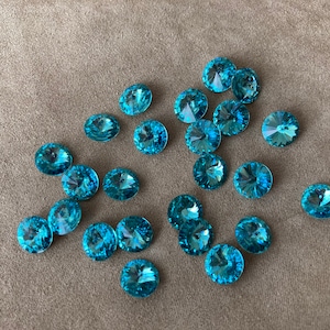 May include: A collection of turquoise blue round rhinestones, scattered on a light brown fabric surface.