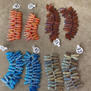 May include: Assortment of glass beads with eye-like patterns. The beads are arranged in four rows, with two rows of orange beads, one row of brown beads, and one row of blue and gold beads. Each row has a label with the size of the beads in millimeters.