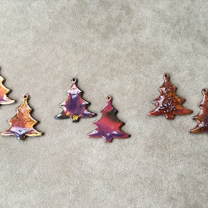 May include: Six handmade Christmas tree ornaments with a glossy, textured finish. The ornaments feature a variety of colors, including orange, red, and purple. Each tree has a small hole at the top for hanging.
