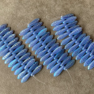 May include: A strand of light blue glass beads with a swirl pattern. The beads are strung on a white thread and are arranged in a staggered pattern.