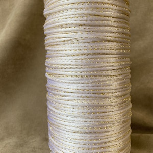 May include: A spool of white cord with a gold metallic thread running through it.