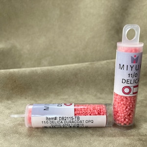 May include: Two small clear plastic tubes filled with pink seed beads. The tubes have labels that read "MIYU 11/0 DELICA" and "Item#: DB2115-TB 11/0 DELICA DURACOAT OPQ GUAVA - APRX 7.2GM/TB".